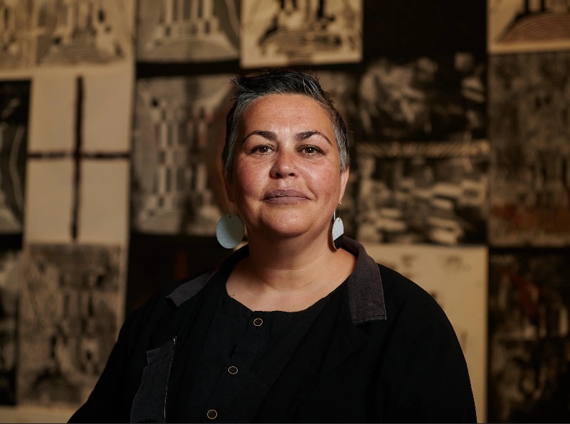 Lisa Waup wearing black, pictured in front of artwork.